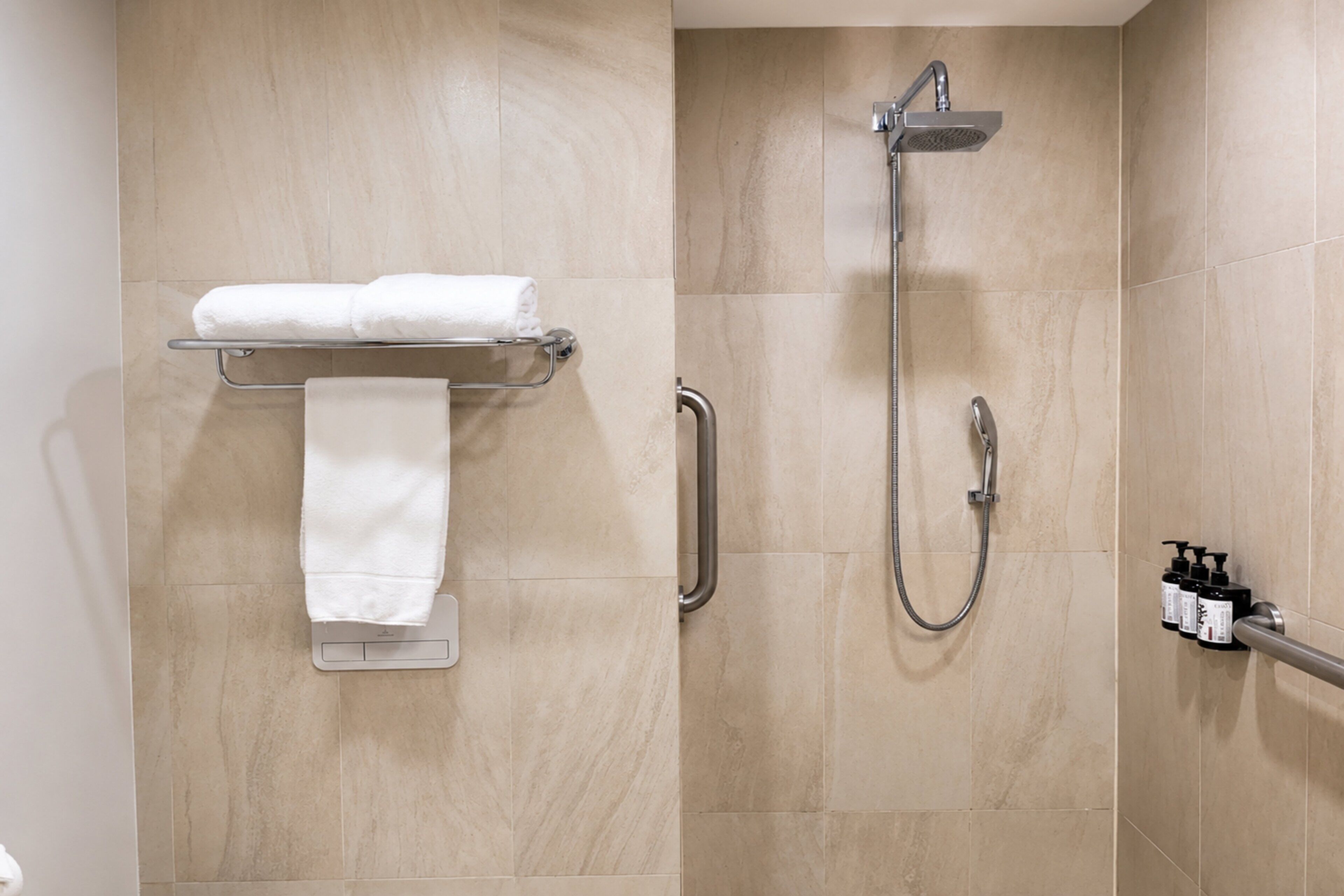 A bathroom with a towel rack, a shower, and a handrail.