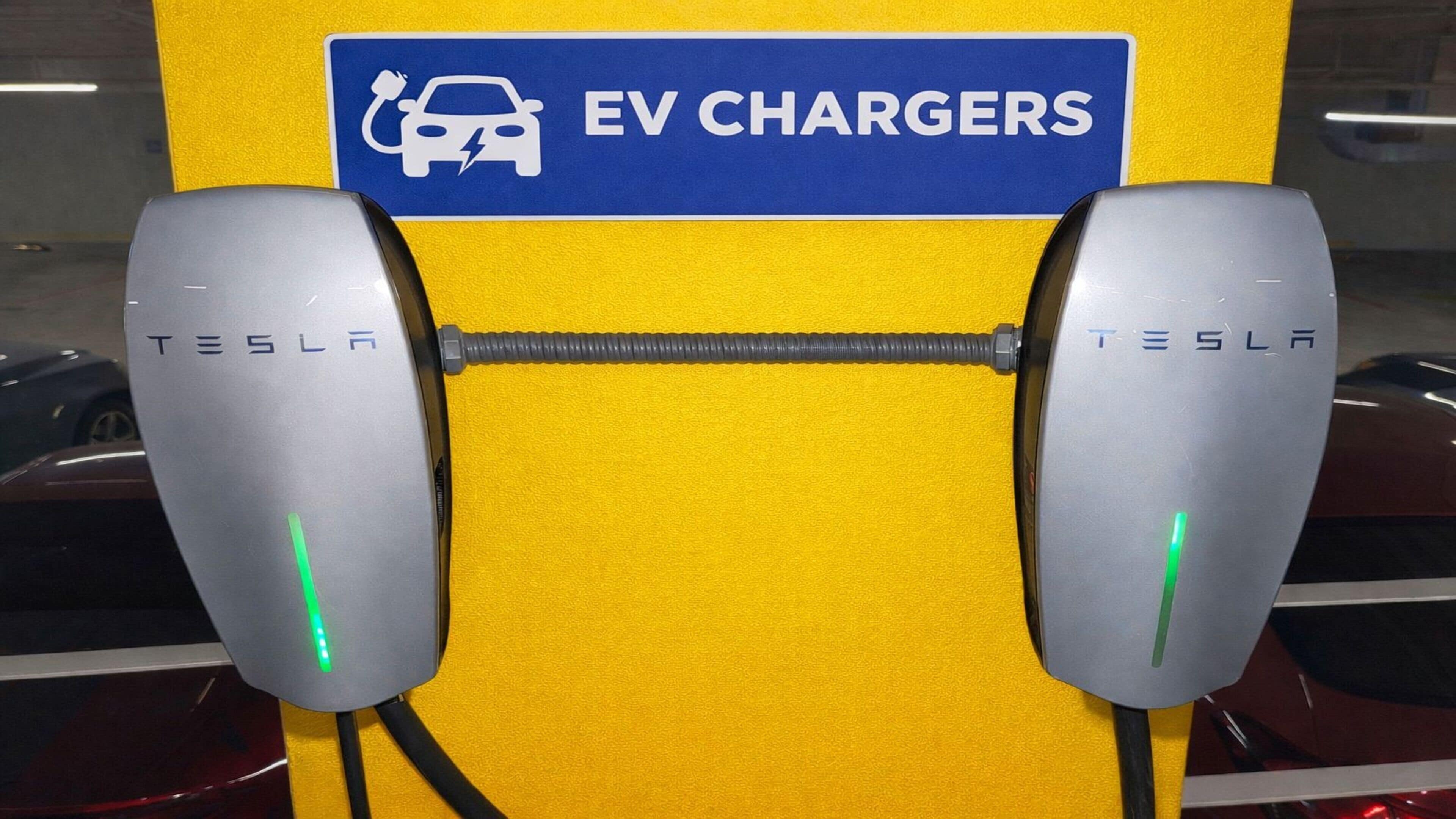 Zwei Tesla-Ladesäulen für Elektrofahrzeuge, darüber ein blaues Schild mit der Aufschrift 'EV CHARGERS'.