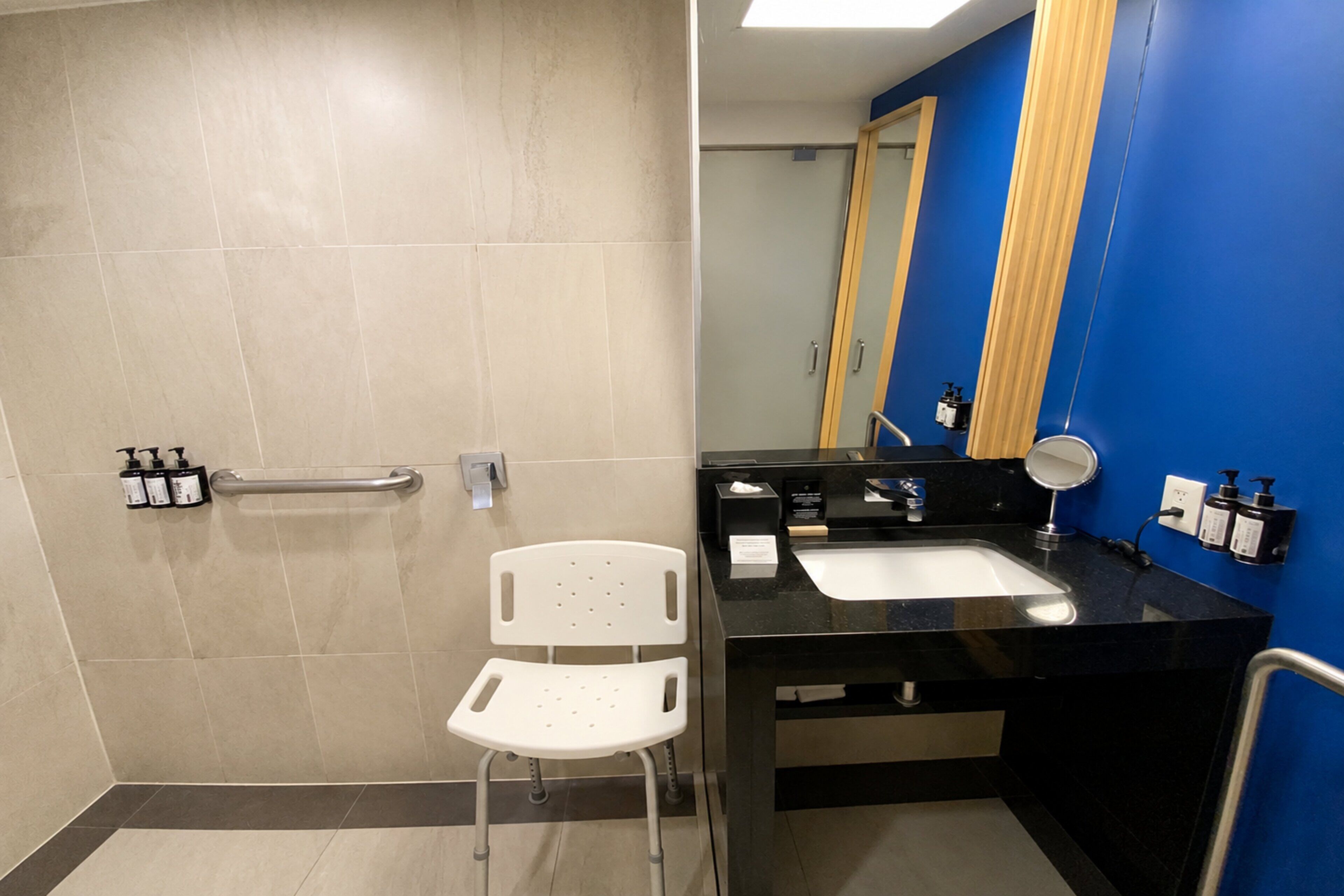 A bathroom with a white chair, a sink, a mirror, and toiletries.