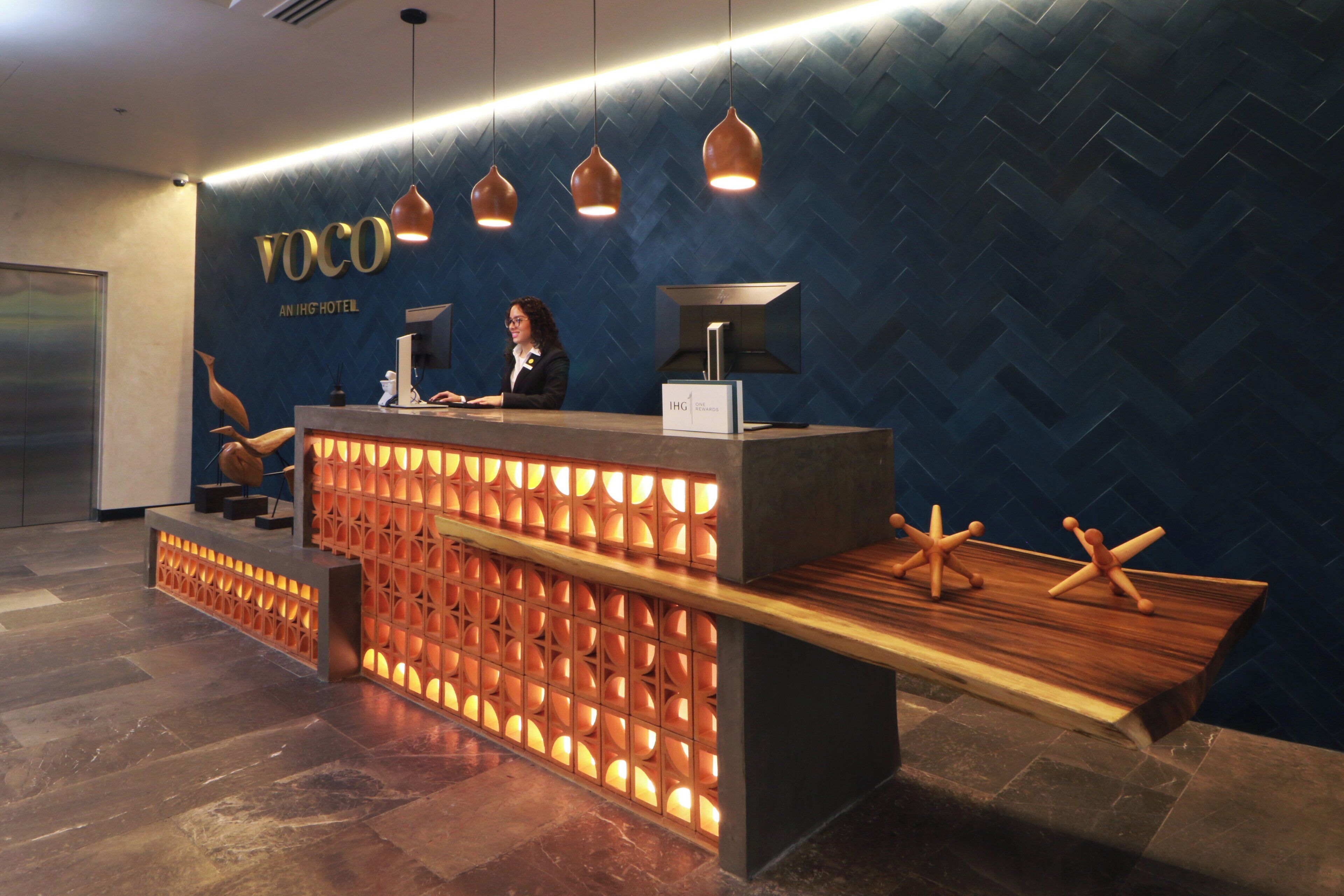 A reception desk with a modern design, featuring a herringbone-patterned wall and pendant lighting.