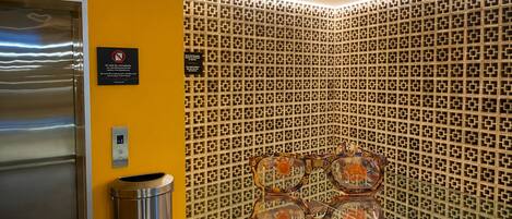 A corner of a hotel lobby with a patterned wall, a trash bin, and a door.