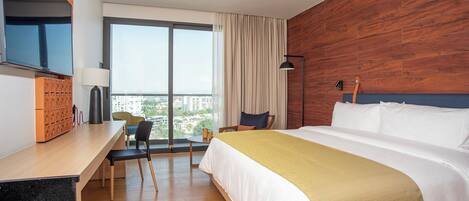 Habitación de hotel con una cama grande, un escritorio, una silla, un televisor y vistas a la ciudad.