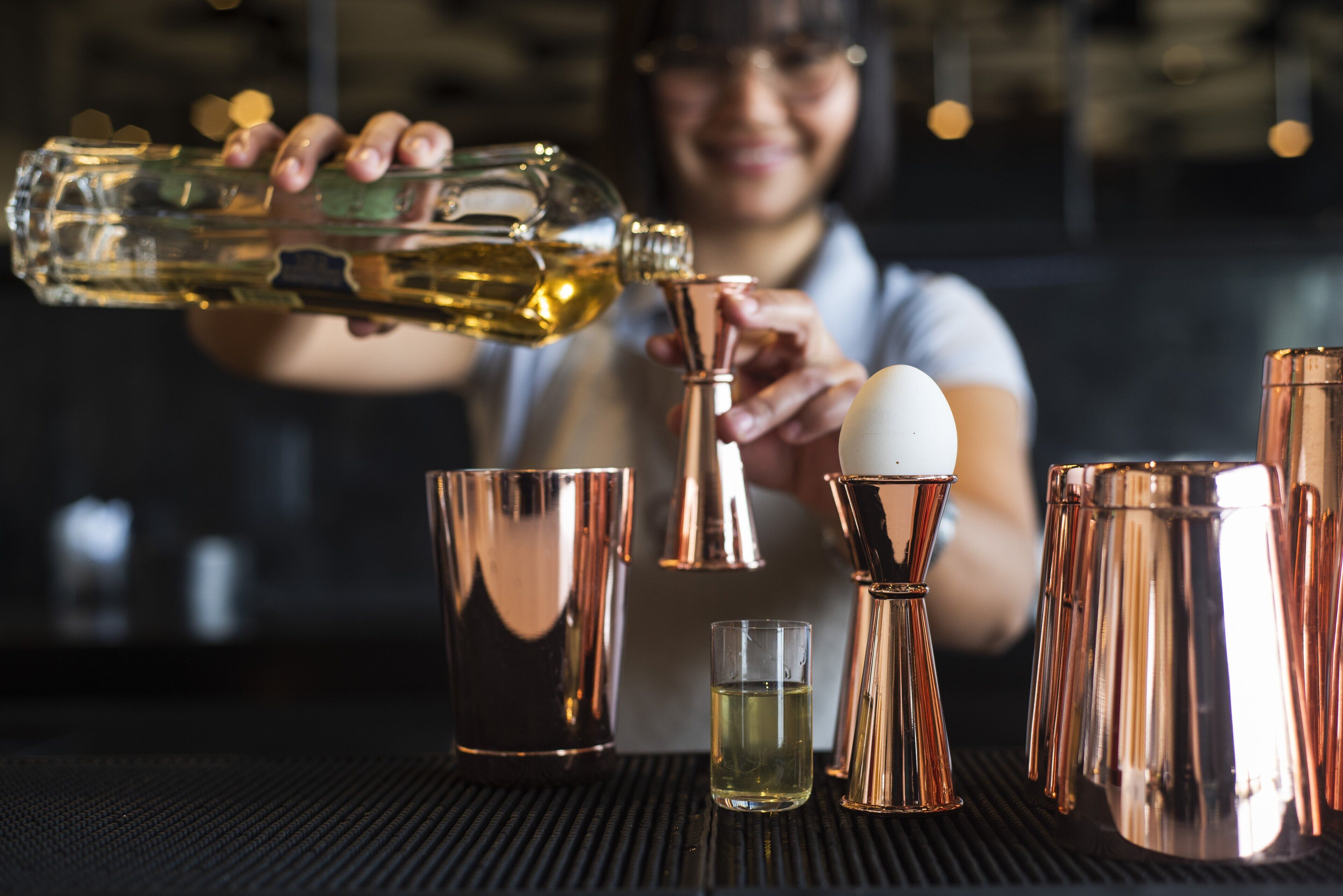 A bartender pouring a drink into a copper shaker.