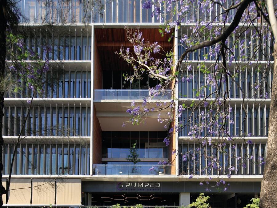 Um edifício moderno com várias varandas, uma placa com 'Pijumped' e vegetação ao redor.