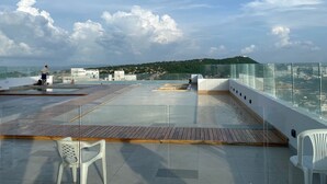 A rooftop terrace with a glass balustrade, wooden decking, and a few plastic chairs. - Beautiful condo with views of the beach (Cartagena)