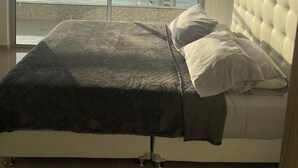 A bedroom with a large window offering a view of the sea and a tall building. - Beautiful condo with views of the beach (Cartagena)