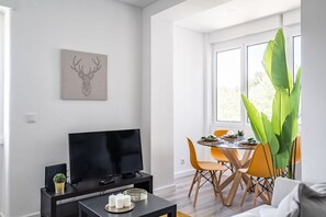 A modern living room with a flat-screen TV, a coffee table with decorative items, a dining area with orange chairs, and a large green plant. - Anato Apartment, Wifi, AC !new! (Lisboa)