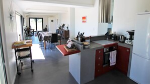 Une cuisine moderne dotée d’un îlot central, d’un coin repas avec une table et des chaises, et d’une grande fenêtre qui laisse entrer la lumière naturelle.