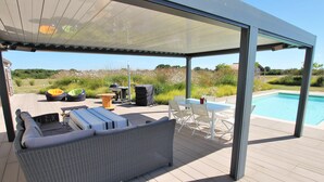 Un espace extérieur aménagé en terrasse, doté d’un coin salon couvert, d’une piscine et offrant une vue sur le paysage environnant.