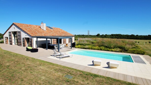 Une maison avec une piscine, un espace salon extérieur et une terrasse couverte.