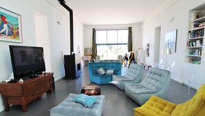 Un salon moderne avec un téléviseur, un canapé bleu, un fauteuil jaune et une bibliothèque.