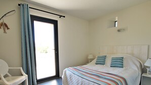 Une chambre à coucher avec un lit, une chaise, une table de chevet, une lampe et une fenêtre avec des rideaux.