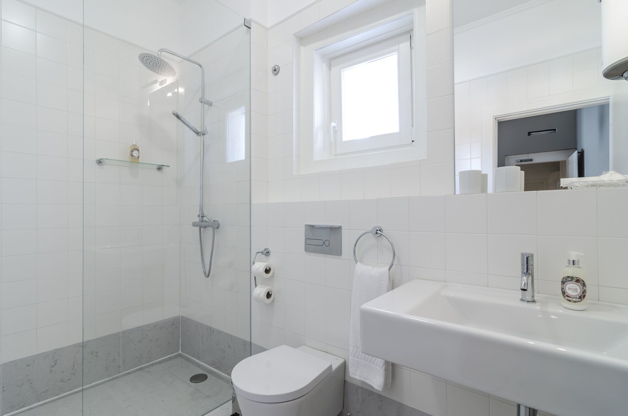 Un baño moderno con ducha de vidrio, inodoro, lavamanos y ventana que proporciona luz natural.