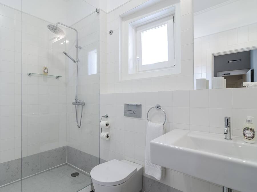 Un baño moderno con ducha de vidrio, inodoro, lavamanos y ventana que proporciona luz natural.