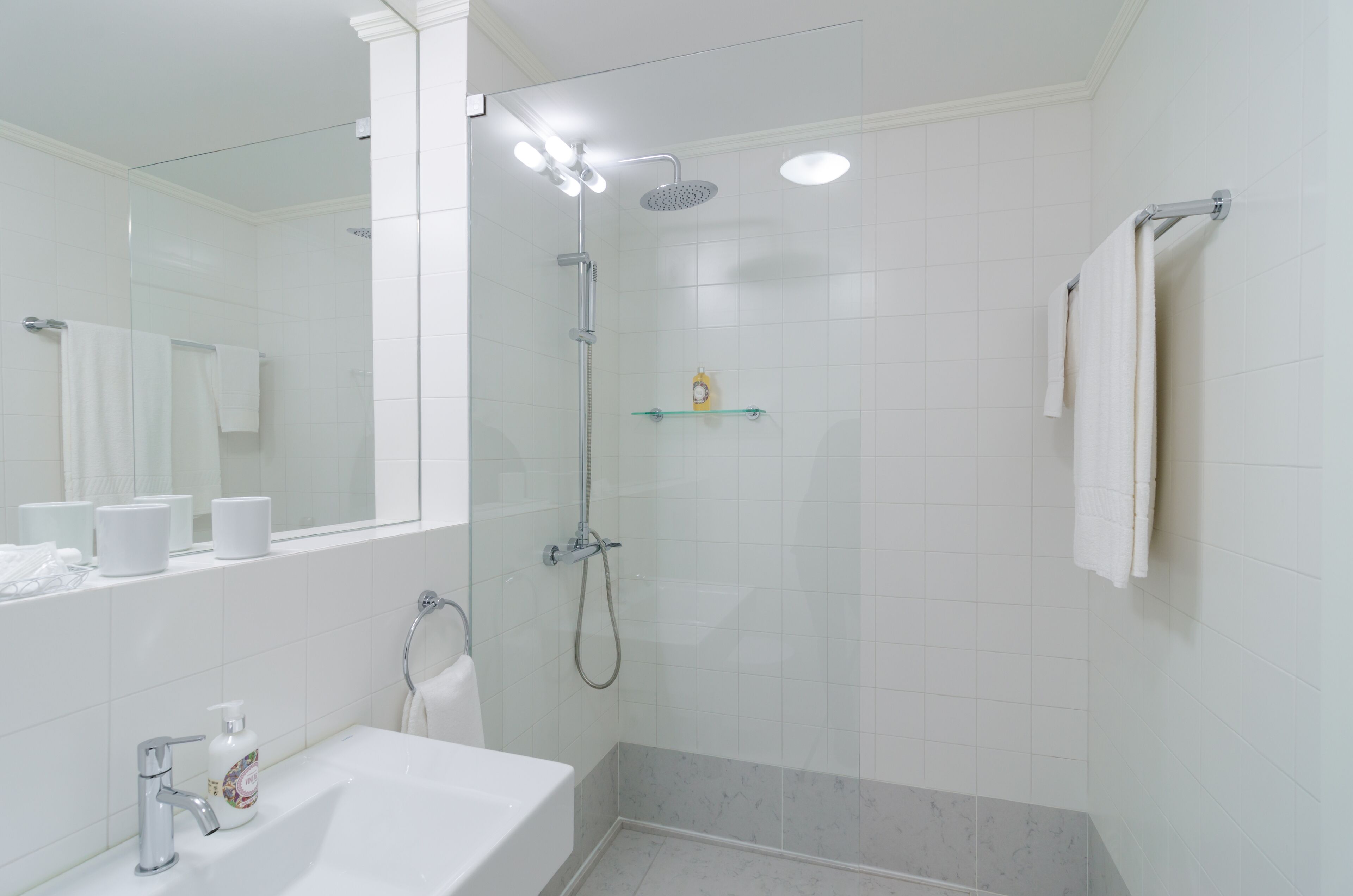 Een moderne badkamer met een douche met glazen wand, een wit wastafelmeubel en een spiegel.