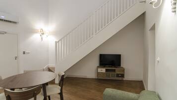 Una sala de estar con una mesa de comedor de madera, un sofá verde, un televisor sobre un mueble de madera y una escalera blanca.