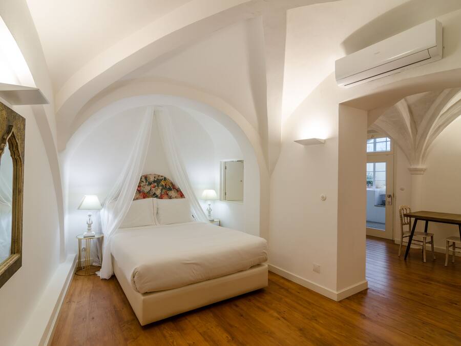 Quarto com uma cama grande, mesa de cabeceira, abajur, espelho e teto em arco.