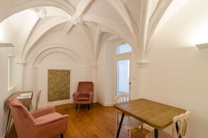 Une pièce dotée d’un plafond voûté, d’une table en bois, d’une chaise rose et d’une autre chaise en bois.
