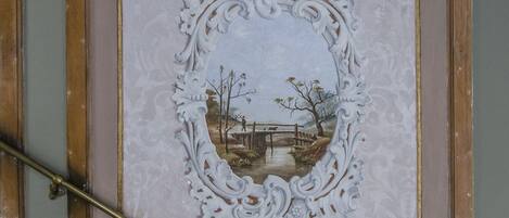 Een decoratief plafond met een sierlijk omlijsting en een landschapsschilderij.