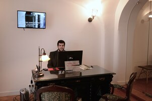 Um homem sentado à mesa com um computador, uma luminária e uma placa na parede.