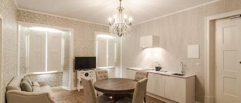 A dining area with a wooden table and chairs, a chandelier, a television, and a kitchen area with a sink and countertop.
