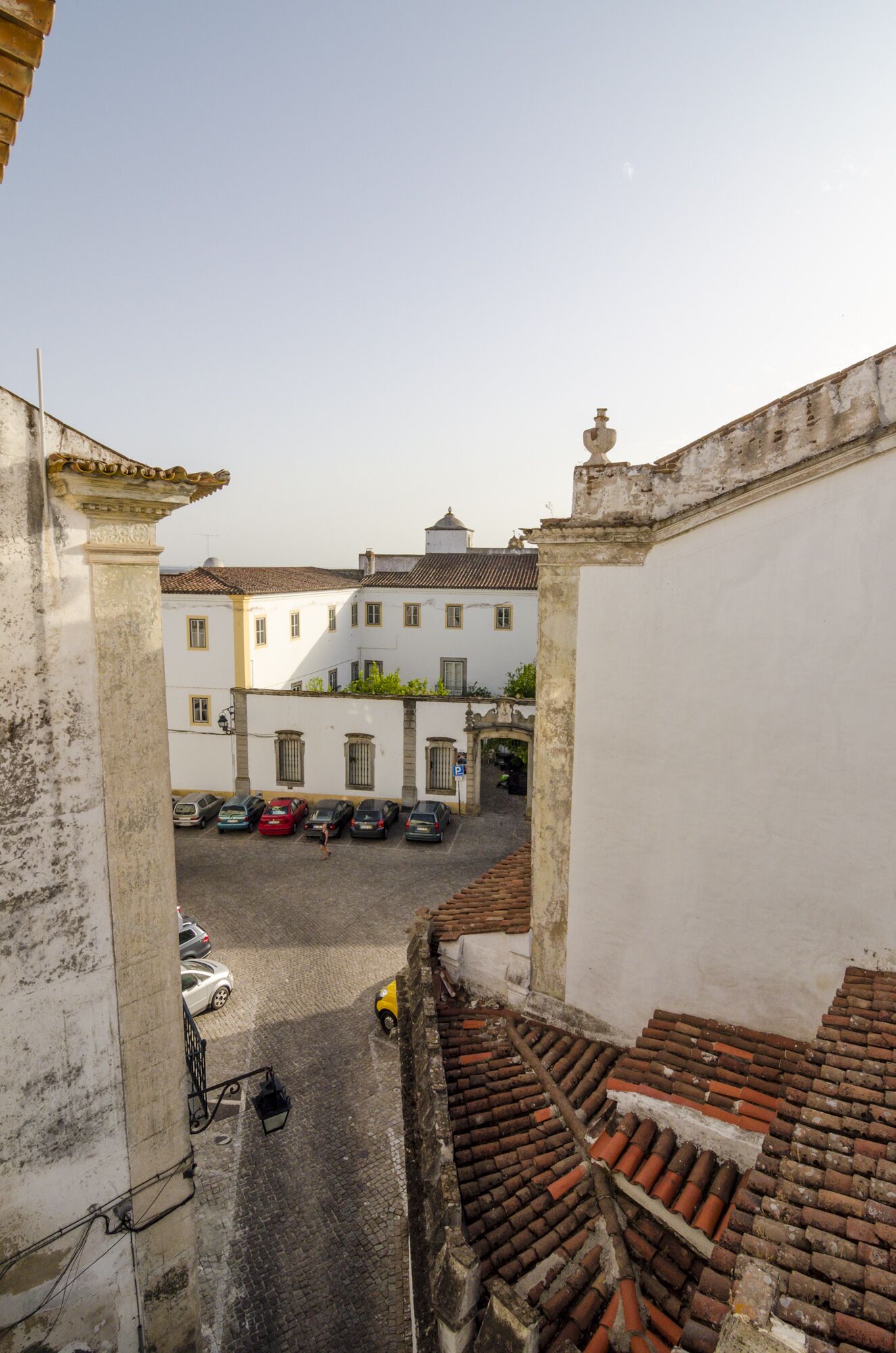 A narrow street with a white building, a tiled roof, and parked cars.