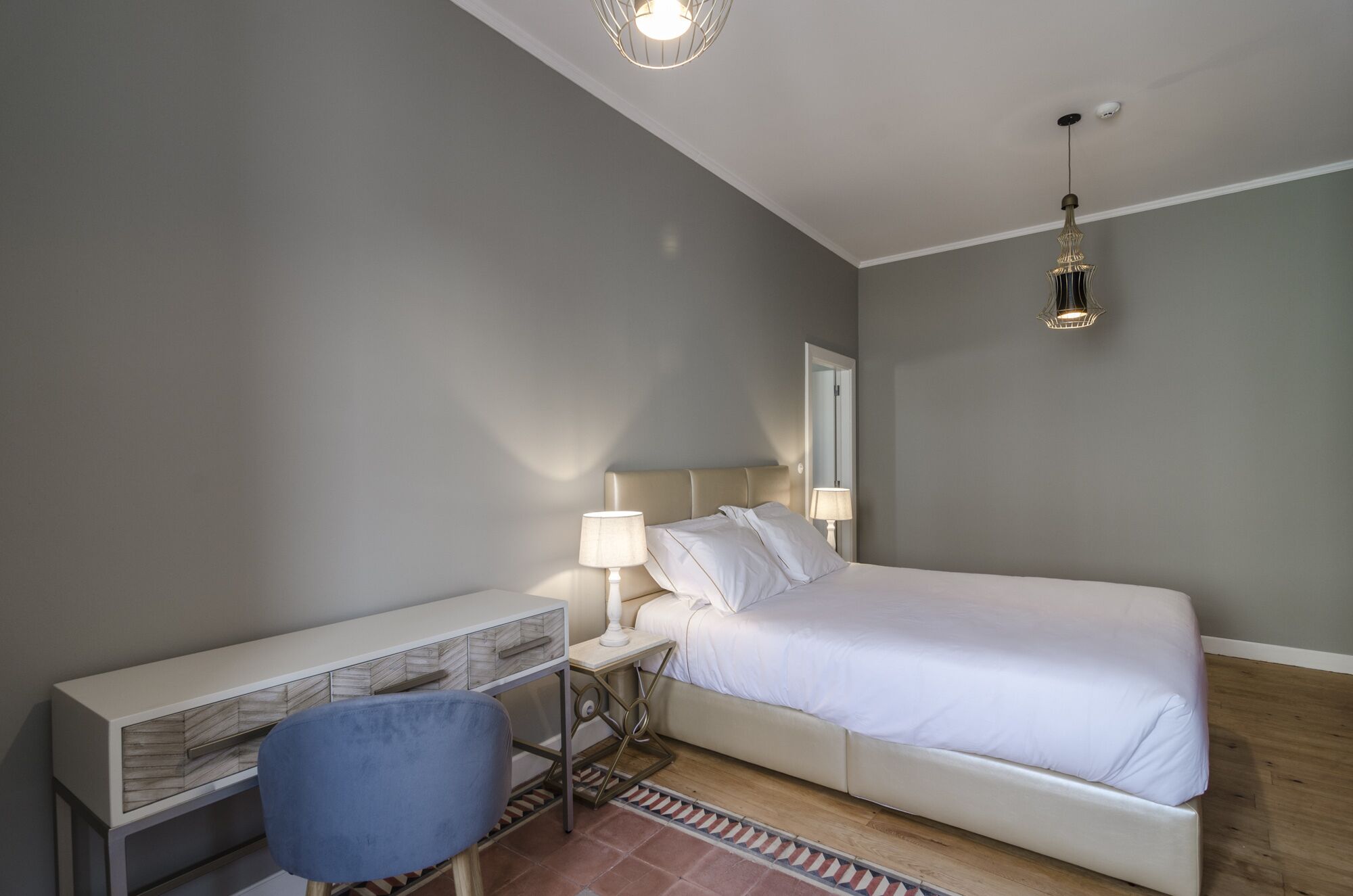 A bedroom with a bed, a desk, a chair, and two bedside lamps.