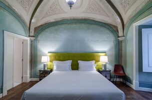 Uma cama grande com lençóis brancos, duas mesas de cabeceira com abajures e um encosto de cabeceira estofado em verde.