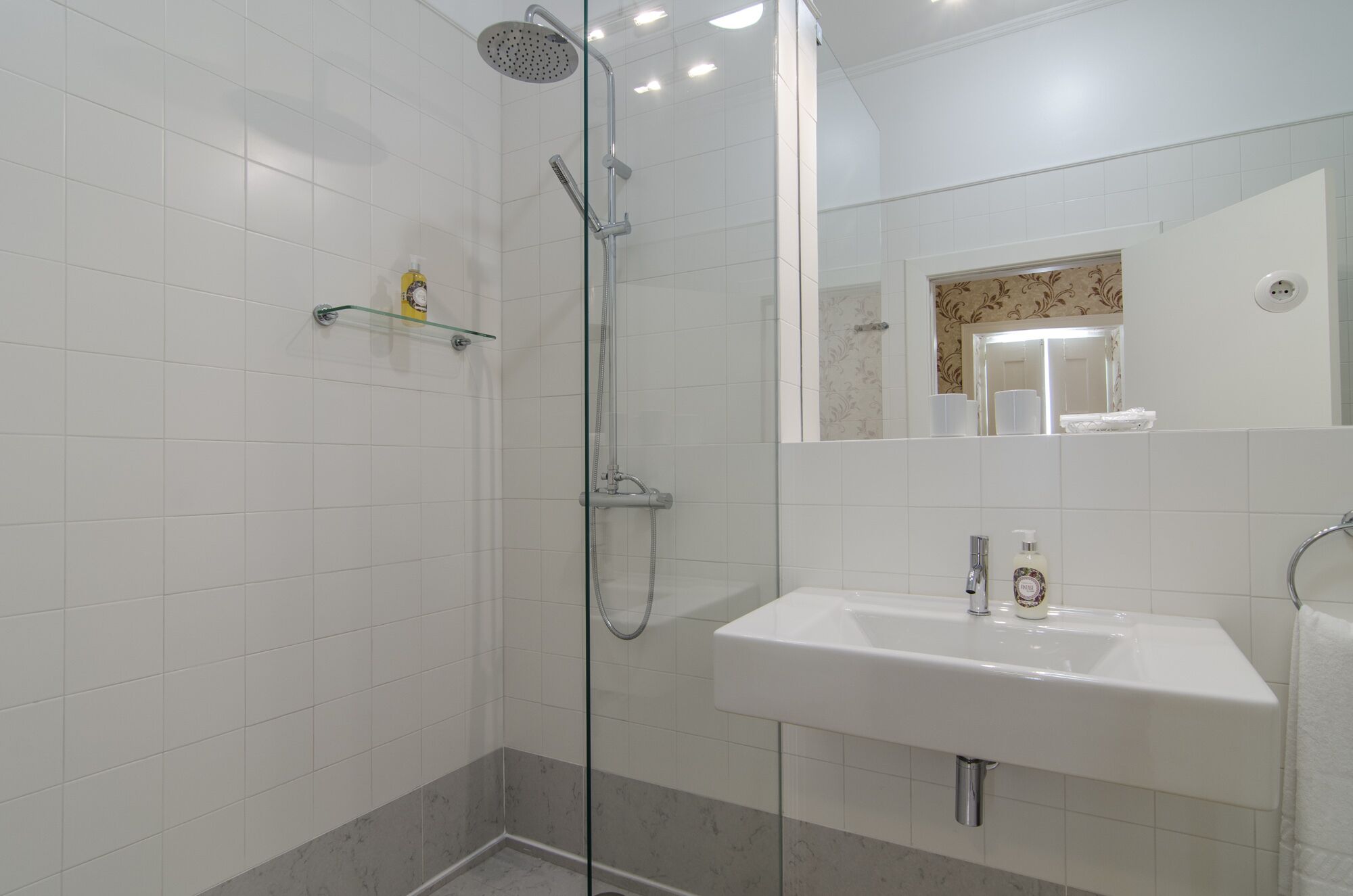 Ein modernes Badezimmer mit einer Duschkabine aus Glas, einem weißen Waschbecken und einem Spiegel darüber.