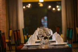 A restaurant table set with plates, glasses, and napkins, with chairs around it. - Pistachio Hotel Sapa (Sa Pa)