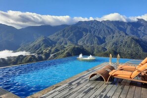 Piscina con cubierta de madera y sillones de descanso con vistas a un paisaje montañoso.