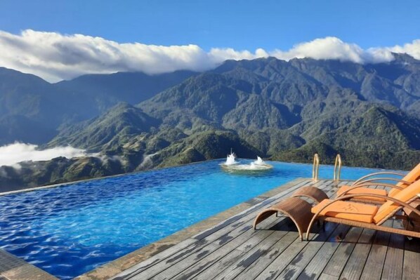 A pool with a wooden deck and lounge chairs overlooking a mountainous landscape. - Pistachio Hotel Sapa (Sa Pa)