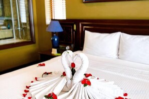 Una cama cuidadosamente hecha con una escultura de toalla y pétalos de rosa.