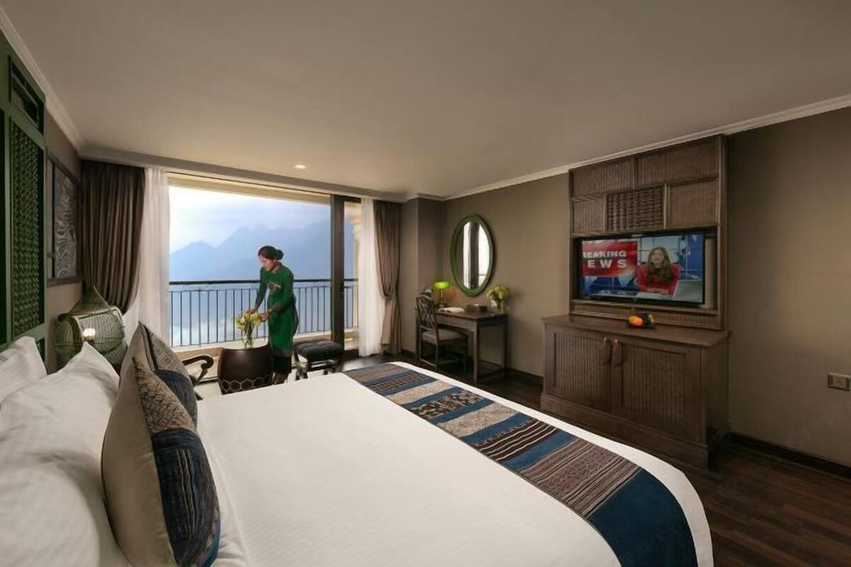 A hotel room with a large bed, a desk, a television, and a view of mountains.