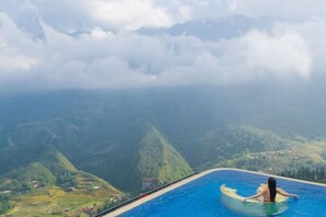 A person sitting on a surfboard in a pool with a mountainous landscape in the background. - Pistachio Hotel Sapa (Sa Pa)