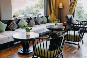 A seating area with a sofa, chairs, and tables, featuring a view through a window. - Pistachio Hotel Sapa (Sa Pa)