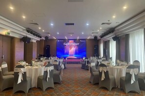 A banquet hall with round tables, chairs, and a stage for presentations. - Pistachio Hotel Sapa (Sa Pa)