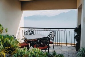 Un balcón con mesa y sillas, vista al mar y una montaña al fondo.