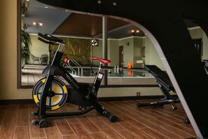Una bicicleta estática en una habitación con un espejo grande que refleja una piscina y una silla.