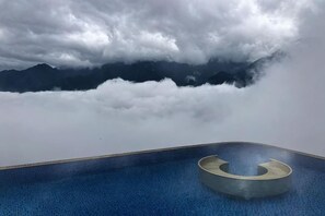 Ein Schwimmbecken mit einem kreisförmigen Element und Blick auf die Berge durch Wolken.