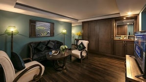 A living room with a sofa, armchairs, a coffee table, and a TV. There are lamps, a painting, and a wooden cabinet. - Pistachio Hotel Sapa (Sa Pa)