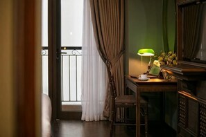 A room with a wooden desk, a chair, a lamp, and a view of a balcony with curtains. - Pistachio Hotel Sapa (Sa Pa)