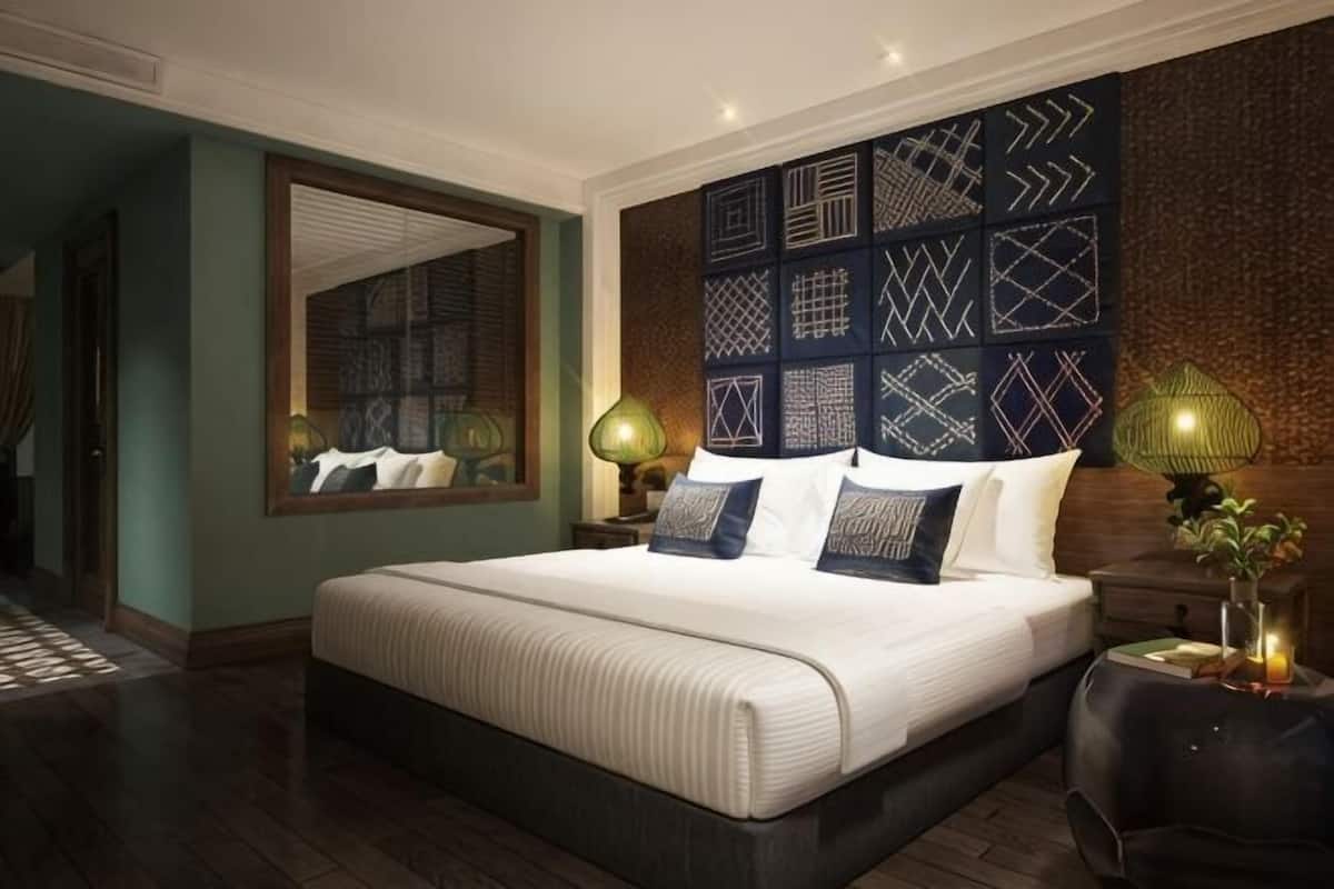 A bedroom with a large bed, a mirror, patterned wall, and two bedside lamps.