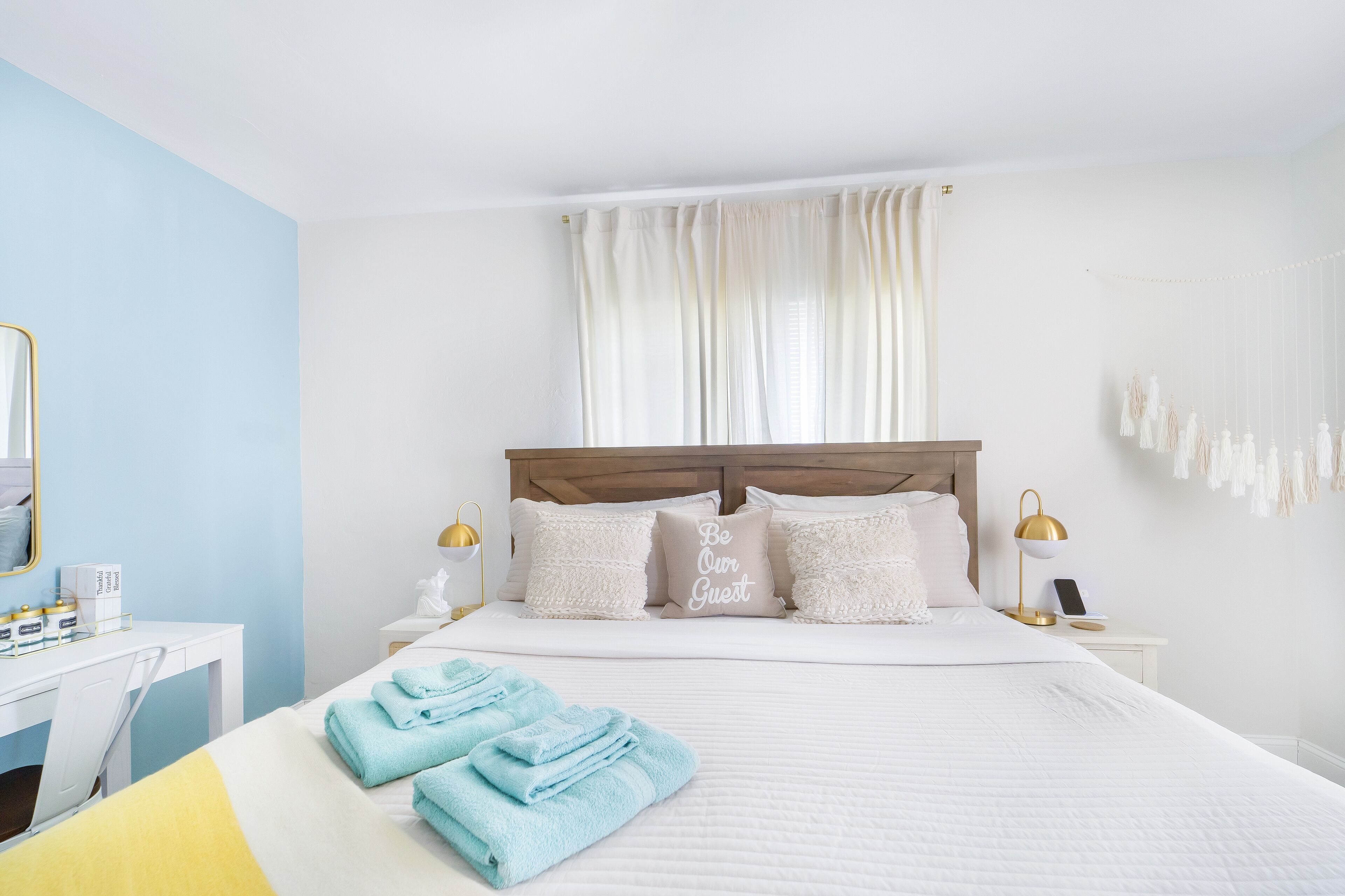 A hotel room with a bed, a desk, and a chair. There are towels on the bed and a lamp on the nightstand.