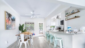 Een lichte keuken met witte kastjes, een houten eettafel en een bar met een 'Relax'-bordje.