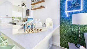 Een moderne keuken met witte kasten, houten planken en een neonbord voor 'Dja Blue Beach House'.