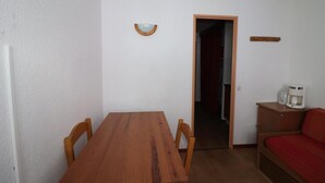 Una stanza piccola con un tavolo e sedie in legno, un divano rosso, una macchina da caffè e una porta che dà su un'altra stanza.