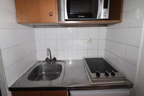 Compact kitchen with a stainless steel sink and microwave oven, along with a wooden cabinet and power outlet.