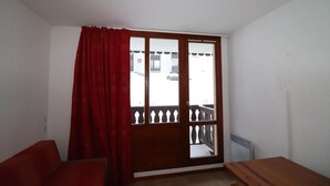Una stanza con un tavolo di legno, un divano rosso e un'ampia finestra vista balcone.