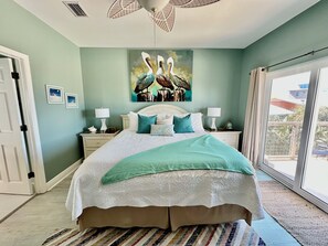 Quarto com cama, duas mesas de cabeceira, um quadro e vista pela janela.